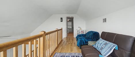 A spacious loft with a wooden staircase, a brown leather sofa, and a patterned rug.