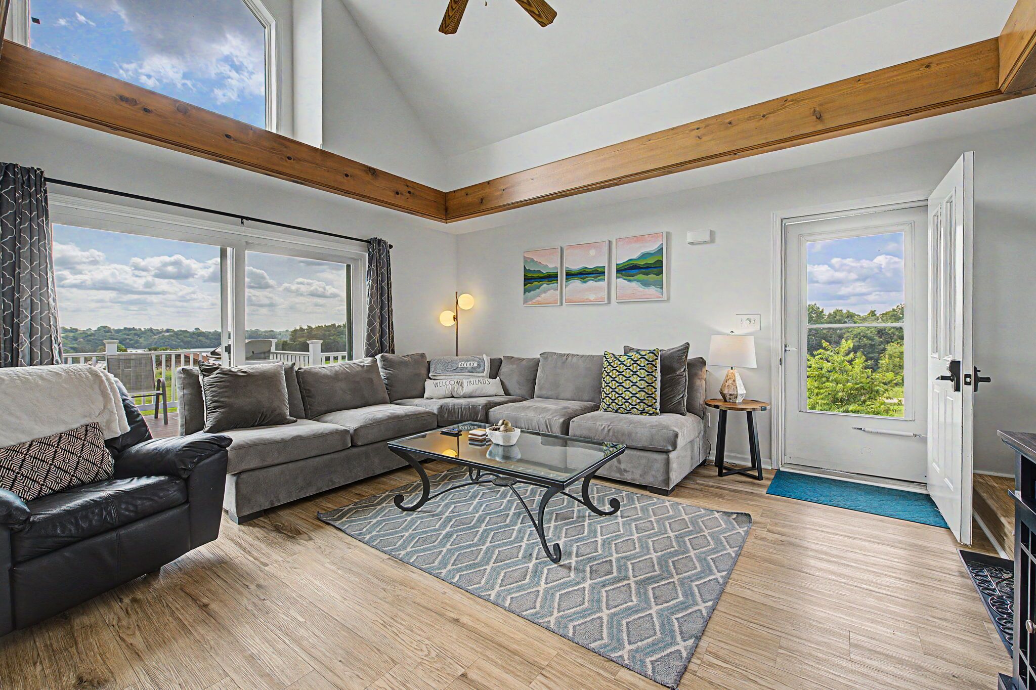 A spacious living room with a large window, a sofa set, a coffee table, and a door leading outside.