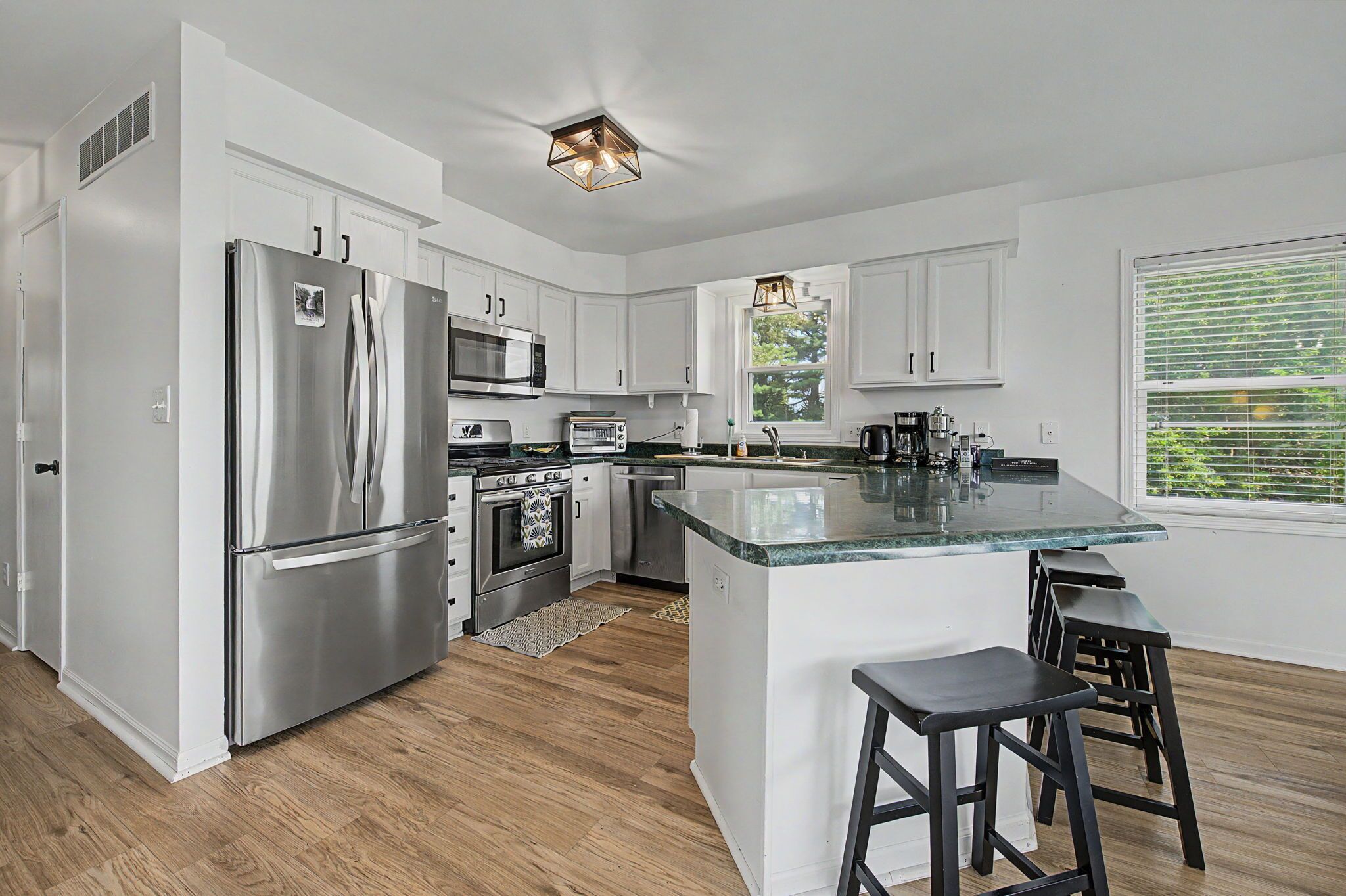 A modern kitchen with stainless steel appliances, a central island with stools, and a window with blinds.