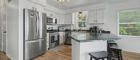 A modern kitchen with stainless steel appliances, a central island with stools, and a window with blinds.