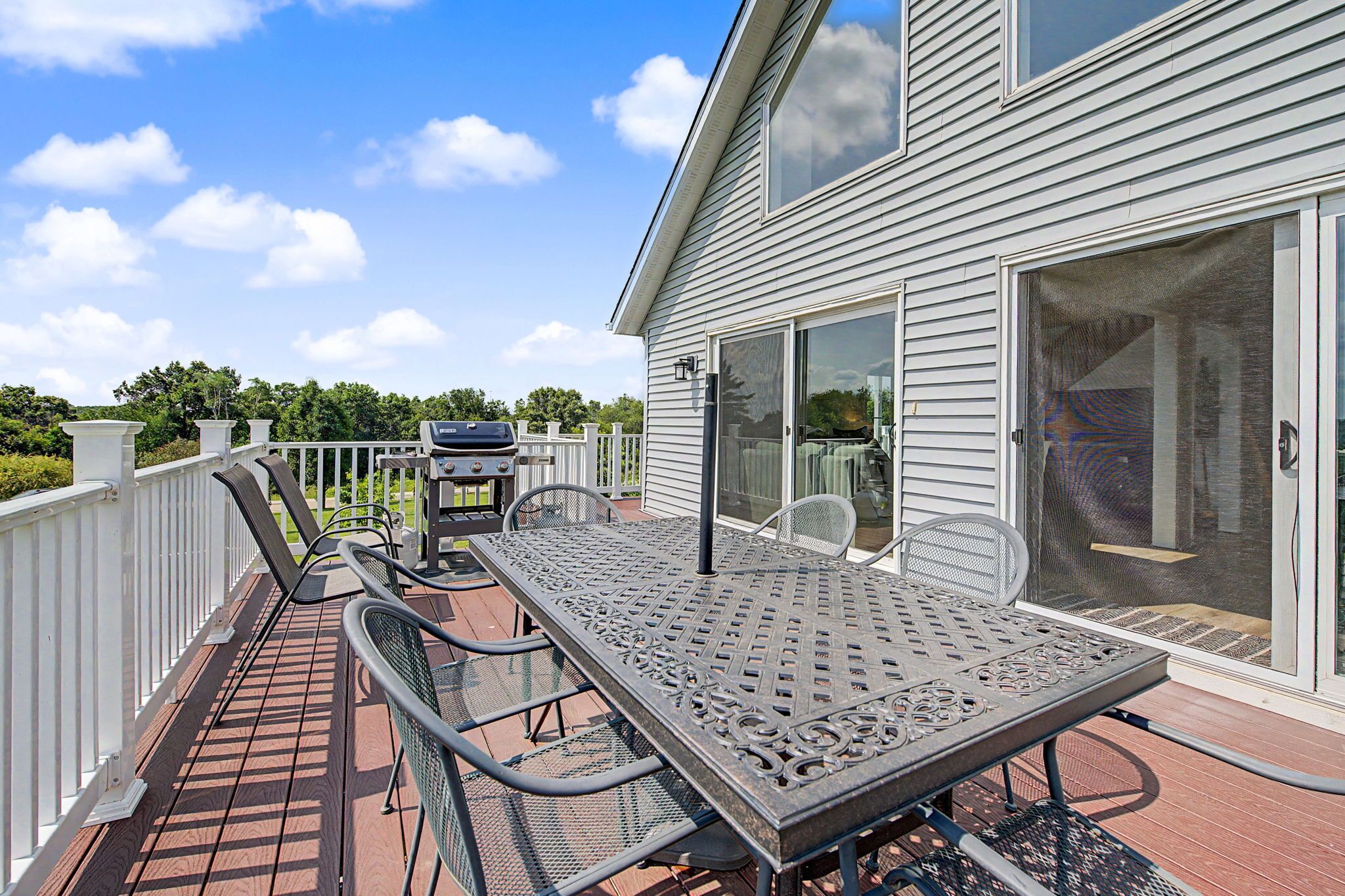 An outdoor patio with a metal table and chairs, a grill, and a sliding glass door leading to a covered area.