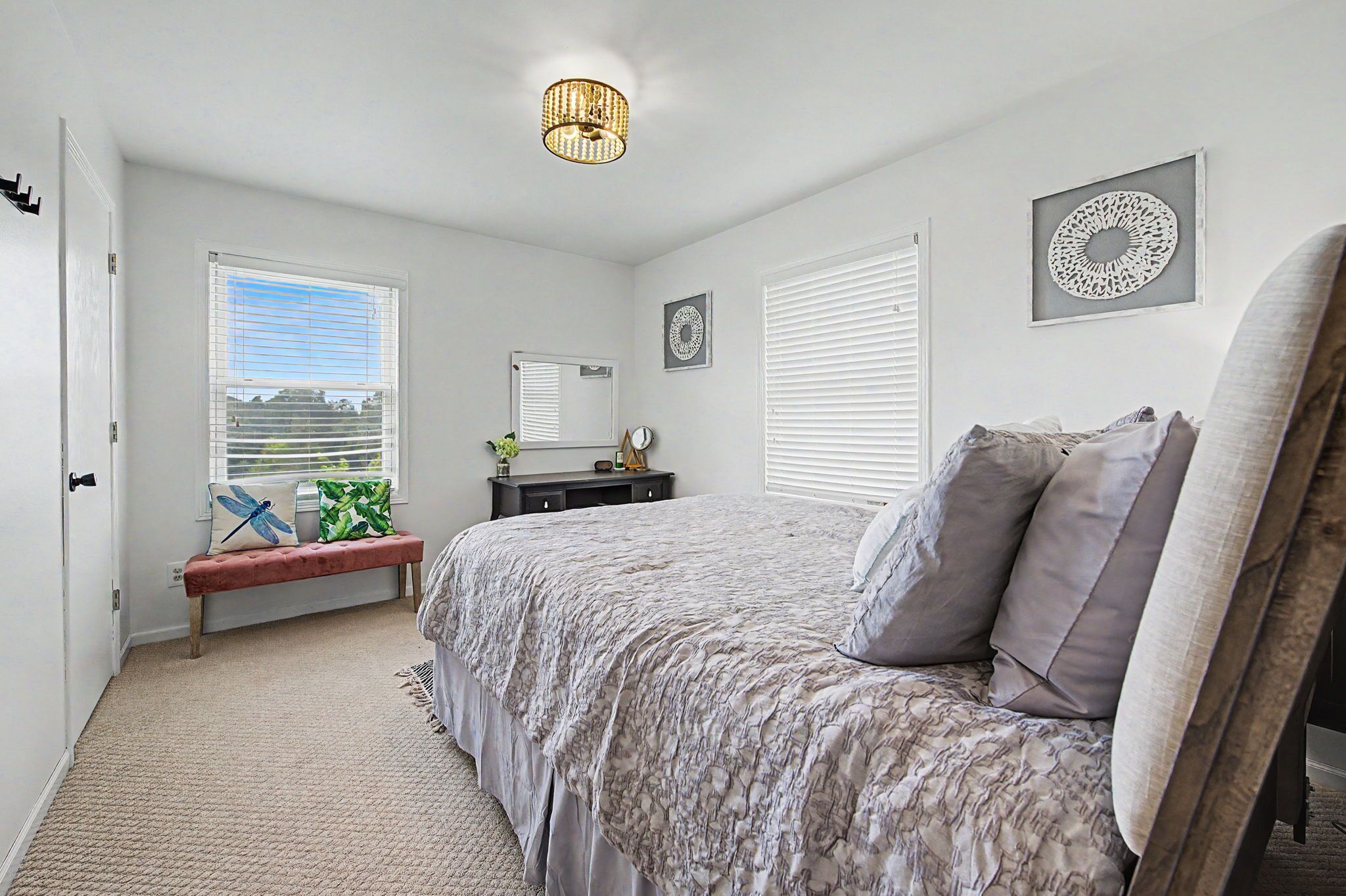 A bedroom with a bed, a bench, a dresser, and a window with blinds.