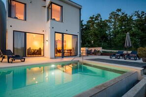 Una casa moderna de dos pisos con piscina, mobiliario exterior y un interior bien iluminado.