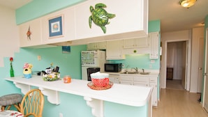 A kitchen with a teal wall, white cabinets, a white countertop, and a wooden chair.