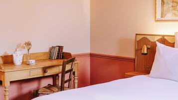 Una habitación de hotel con un escritorio de madera, una silla, una cama y una mesita de noche con lámpara.