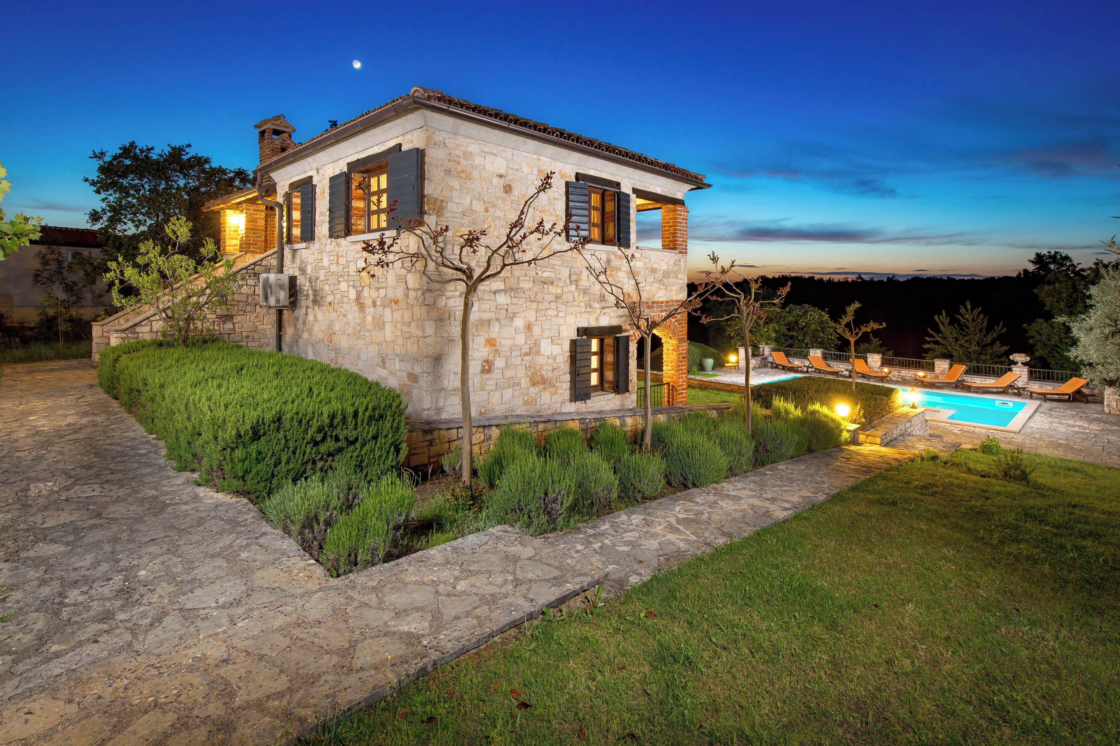 A stone house with a swimming pool, surrounded by a well-maintained garden and a clear view of the night sky.