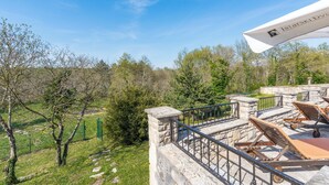 A terrace with stone railings, wooden lounge chairs, and a view of a green landscape.