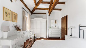 A bedroom with a large bed, white furniture, a wooden ceiling, and a window with curtains.