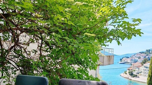 A balcony with two chairs and a table, overlooking a coastal town and a body of water.