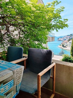 A balcony with two chairs and a table, overlooking a coastal town and a body of water.