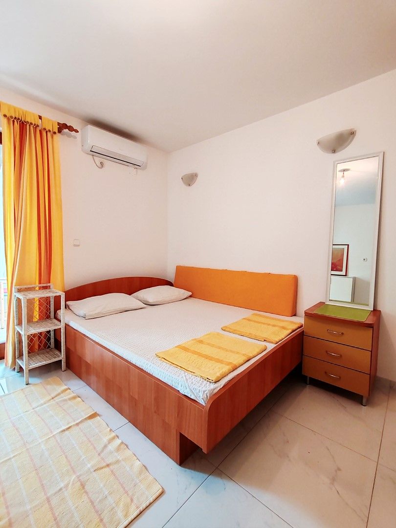 A bedroom with a bed, a bedside table, a mirror, and a window with curtains.