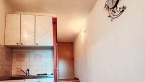 A compact kitchen with a refrigerator, cabinets, and a clock on the wall.