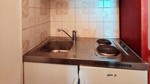 A compact kitchen with white cabinets, a stainless steel sink, and a built-in refrigerator.