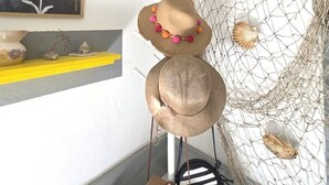 A room with a white wall, a yellow shelf, a framed painting, and a netted area with hats and a small basket.