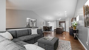 Una sala moderna con un sofá seccional gris, un reposapiés y un comedor al fondo.
