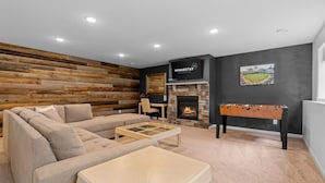 Una sala de estar moderna con un sofá seccional, una mesa de fútbol, una chimenea y un televisor montado en la pared.