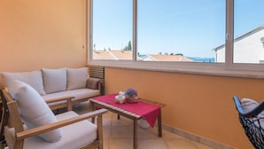 Un balcon avec un canapé, une petite table recouverte d’une nappe rouge et une chaise.