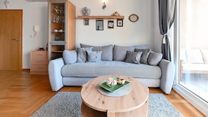 Un salon moderne avec un canapé gris, une table basse en bois et un meuble vitré contenant des objets décoratifs.