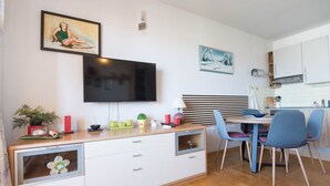 Une cuisine moderne avec un coin repas, comprenant un téléviseur à écran plat, des armoires en bois et une table à manger avec des chaises.