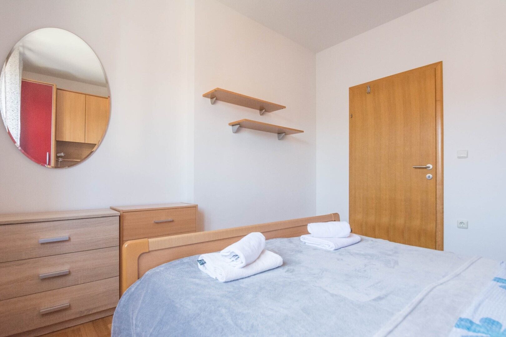 A bedroom with a bed, a wooden dresser, a mirror, and a door.