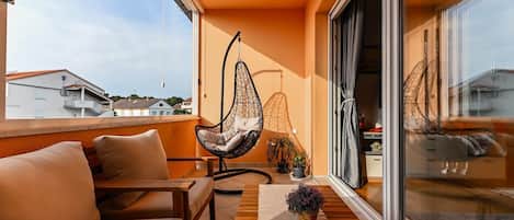 Un balcon avec un canapé, un fauteuil suspendu et des plantes en pot.