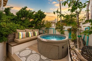 A hot tub with a beige exterior, a beige sofa with colorful cushions, and a patterned rug.