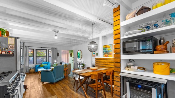 A modern kitchen with a dining area, wooden flooring, and a view to the outside.