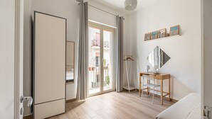 Una habitación moderna con una puerta corredera que da a un balcón, un escritorio con una silla y una lámpara colgante.