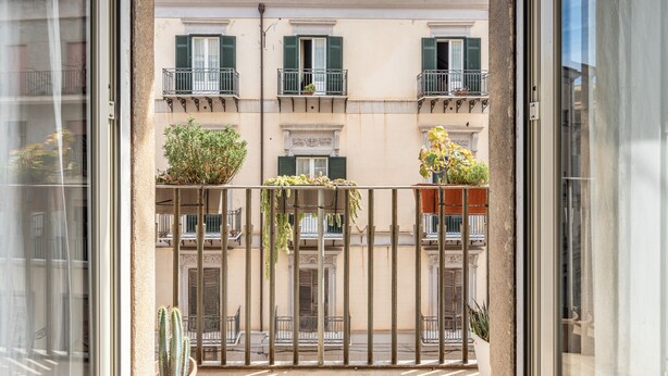 Un balcón con vistas a un edificio con varias ventanas y balcones, algunos con plantas.