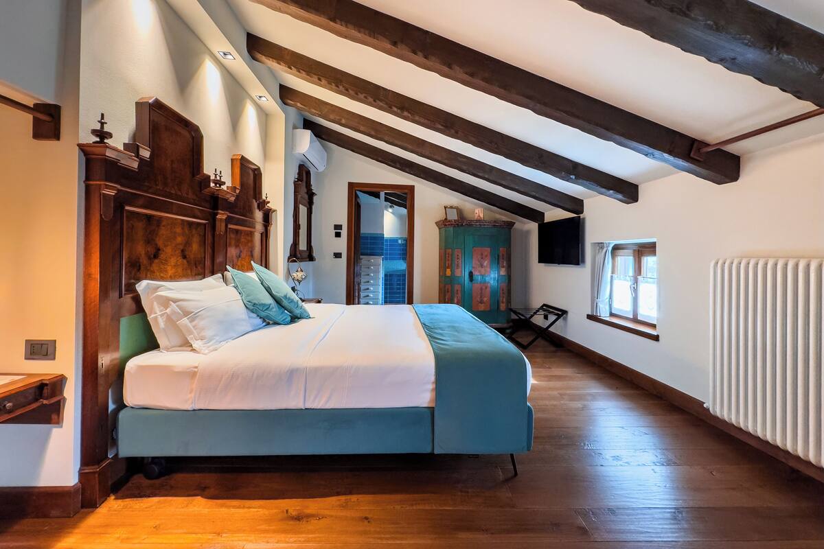 Un dormitorio con cama, vigas de madera, radiador y ventana.
