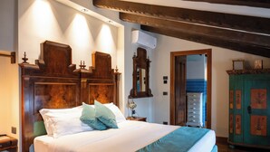 Un dormitorio con cabecera de madera, cama con ropa de cama blanca y turquesa, mesita de noche con lámpara, cómoda y espejo.