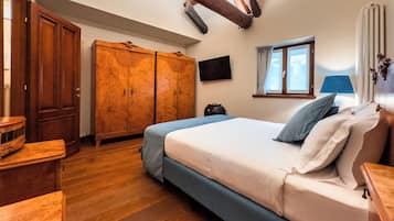 Quarto com guarda-roupa de madeira, cama com roupa de cama azul, janela com cortinas e televisão de tela plana na parede.