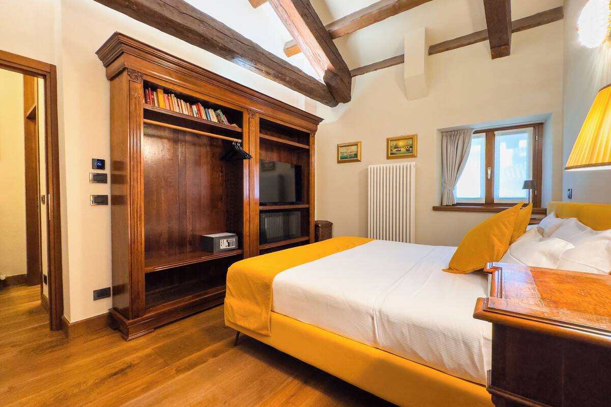 Un dormitorio con un armario de madera, una cama con ropa de cama amarilla, una mesita de noche de madera y una ventana con cortinas.