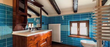 Um banheiro com azulejos azuis, armários de madeira, um radiador branco e uma janela.