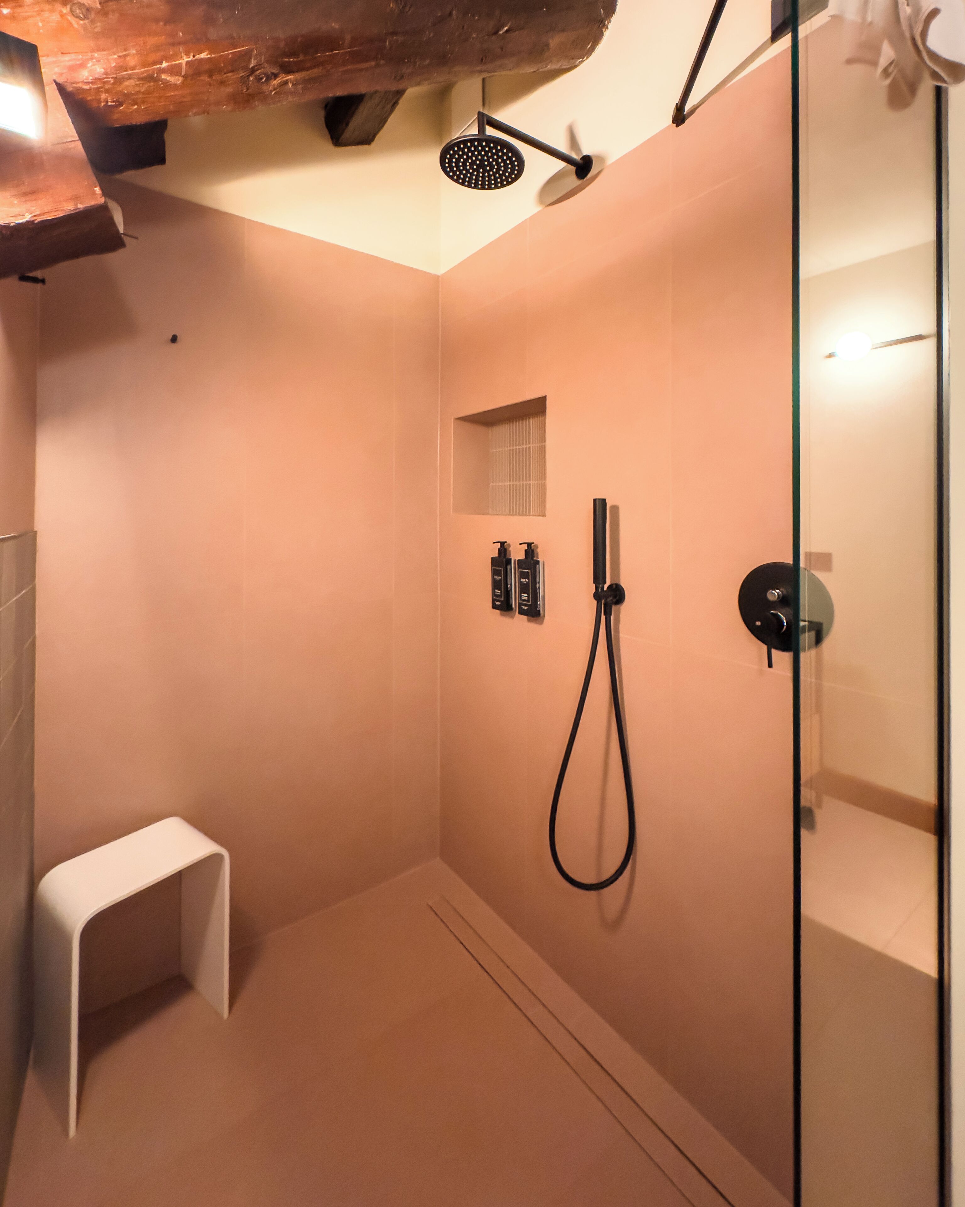 Un'area doccia moderna con porta in vetro, soffione a mano e piccolo ripiano con articoli da toilette.