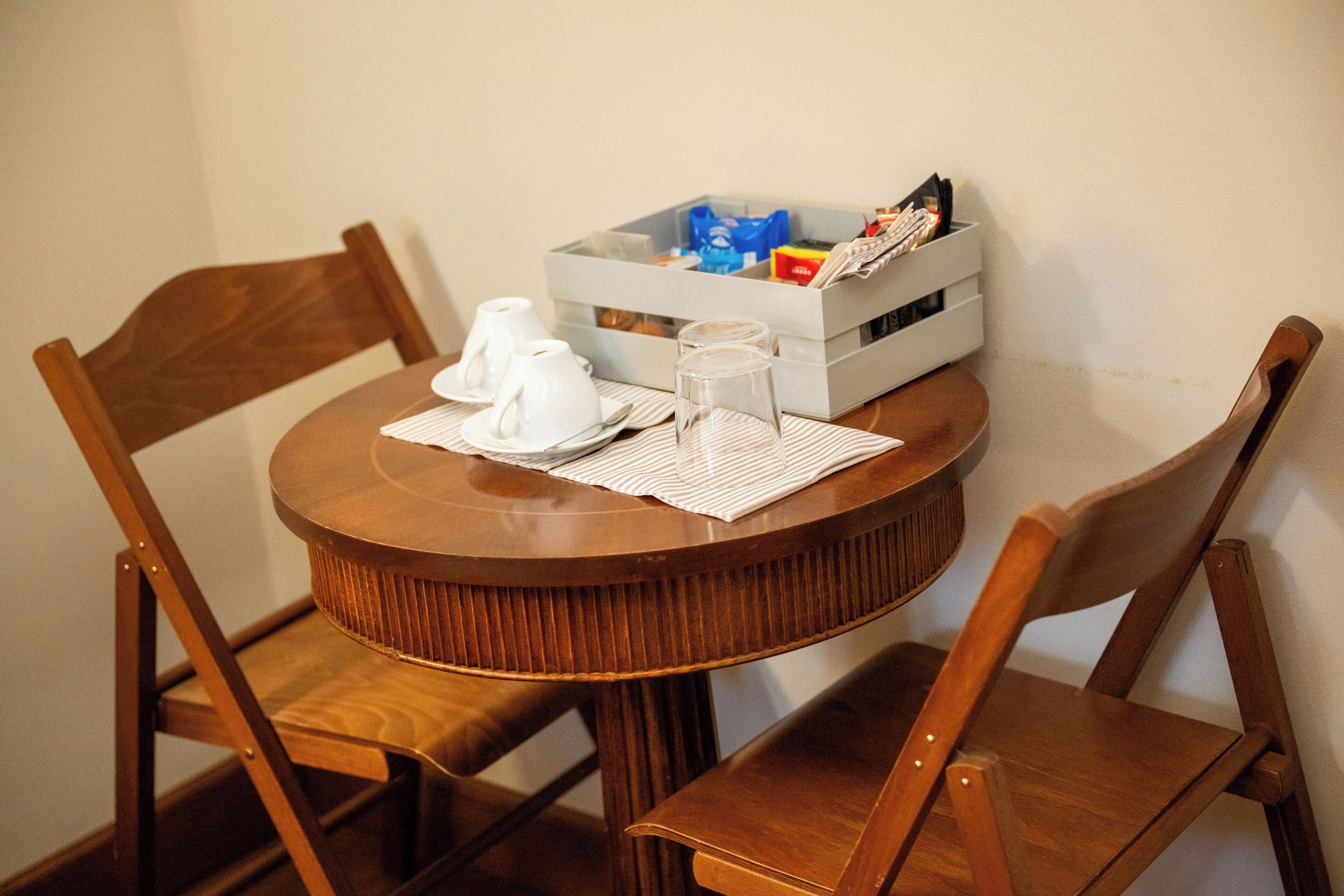 Ett runt träbord med två vita koppar och ett glas, tillsammans med en vit bricka och en låda med diverse toalettartiklar.