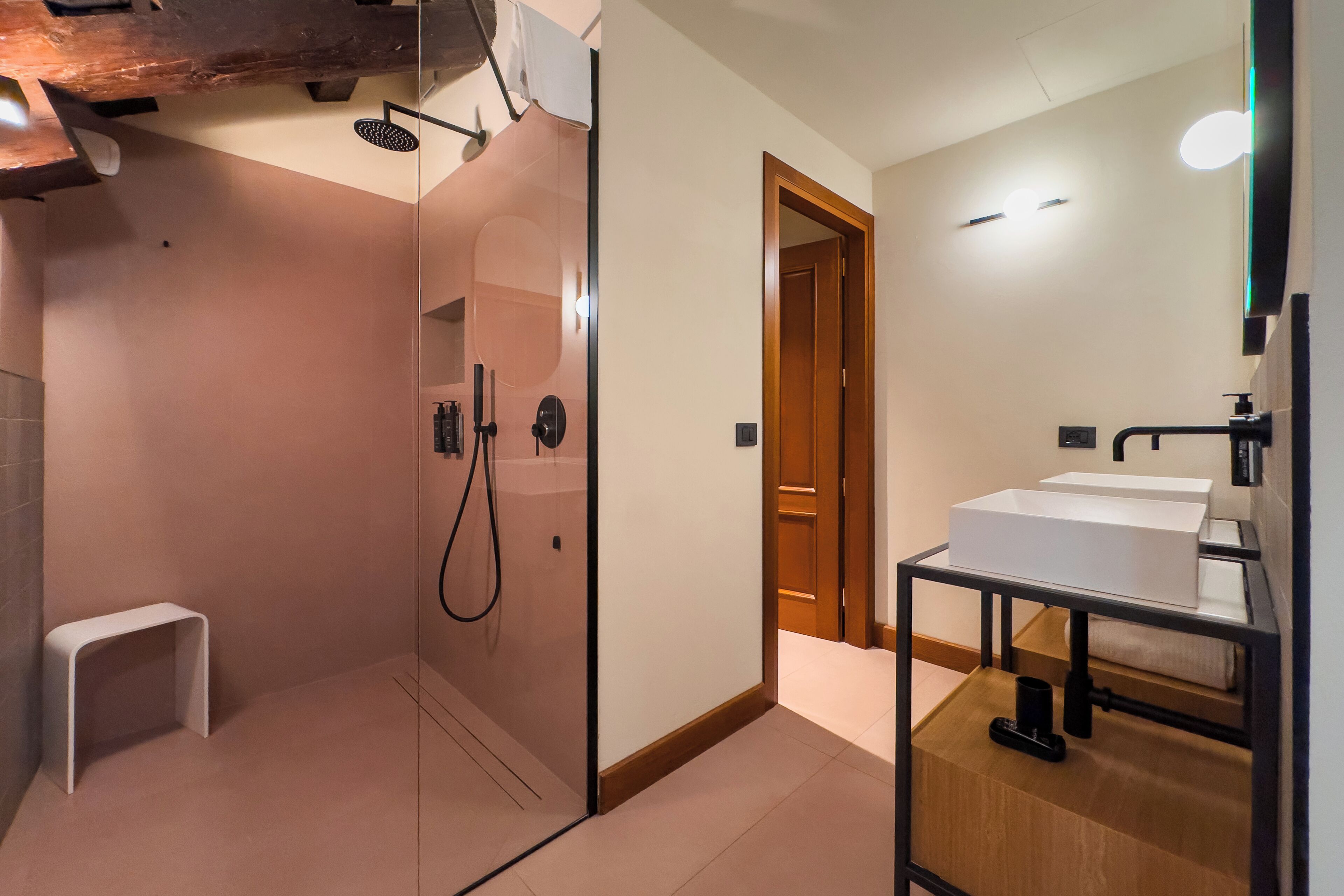 Een moderne badkamer met een glazen douchecabine, een houten bankje en een wastafel met spiegel.