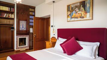 A bedroom with a large bed, a bookshelf, a fireplace, and a painting on the wall.