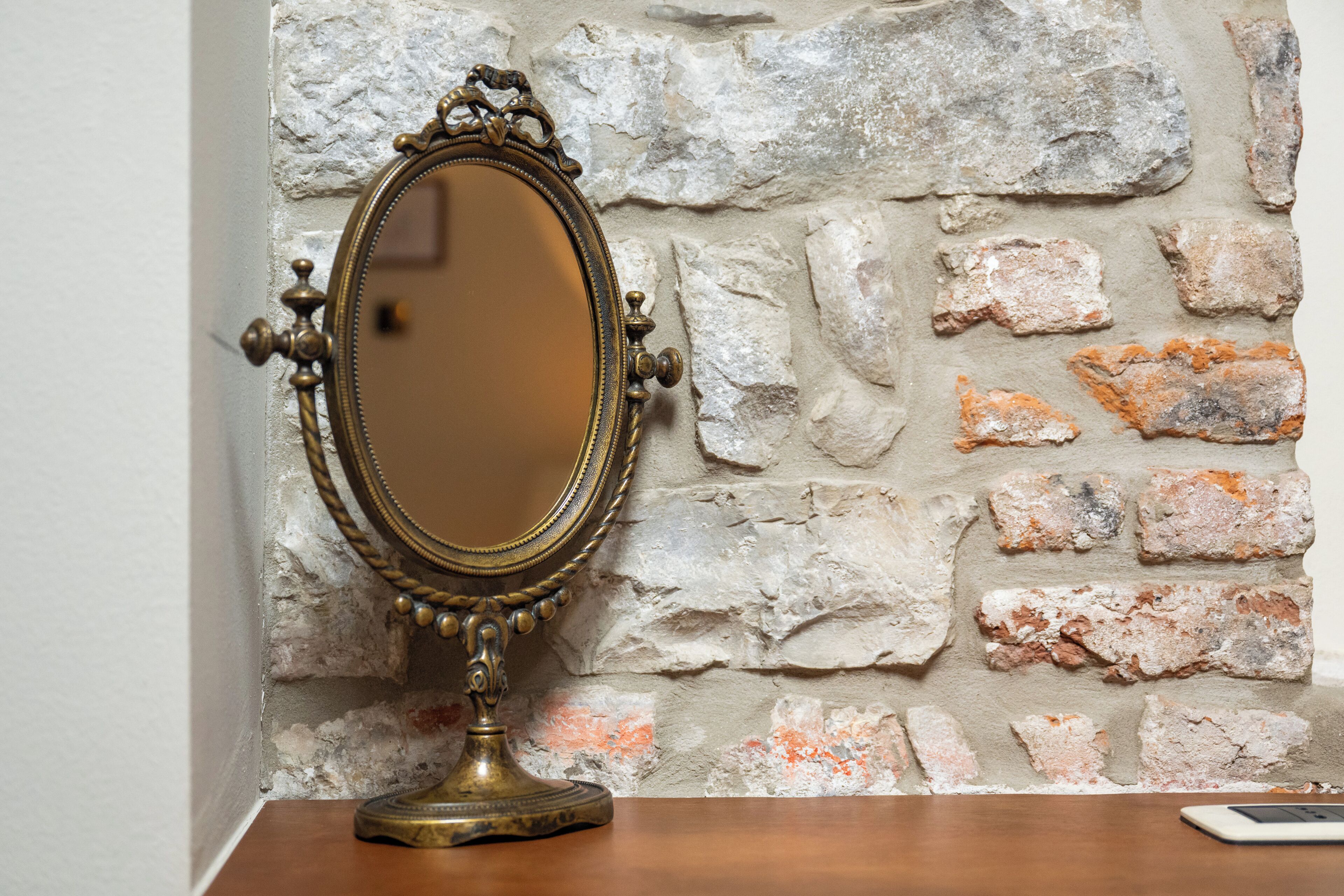 A mirror with an ornate frame on a wooden surface against a stone wall.