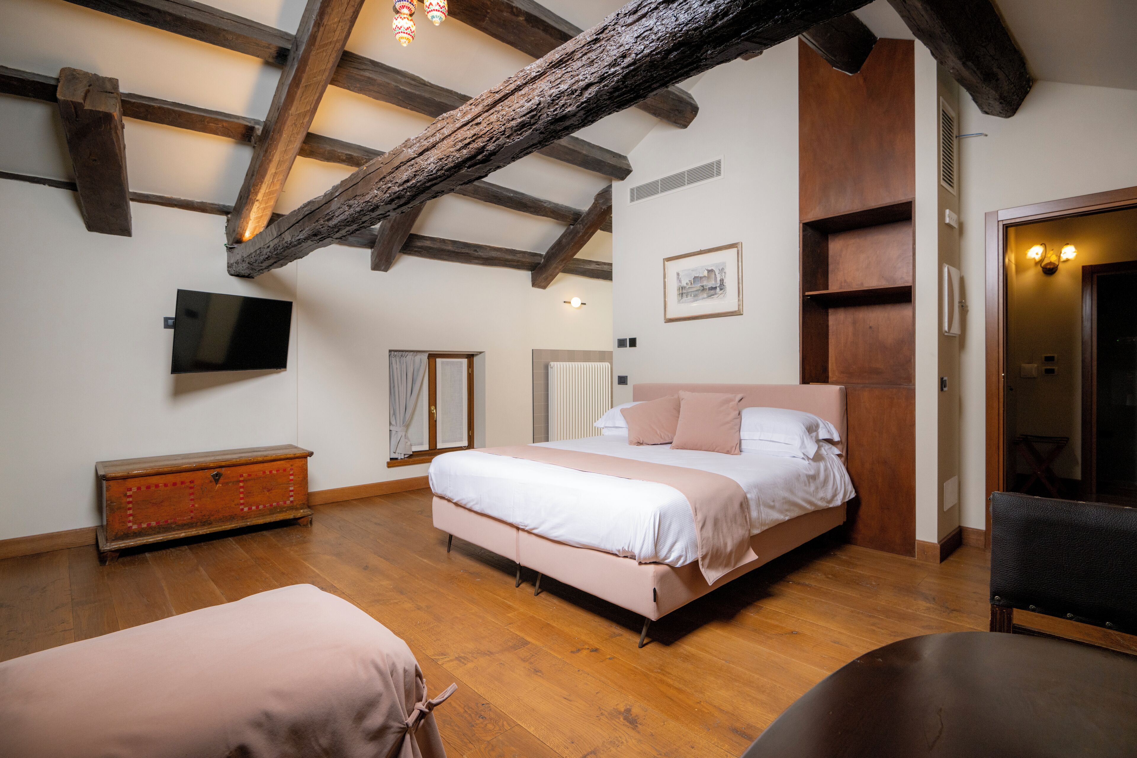 Un dormitorio con una cama grande, vigas de madera, un aparador, un televisor y una puerta con luces.