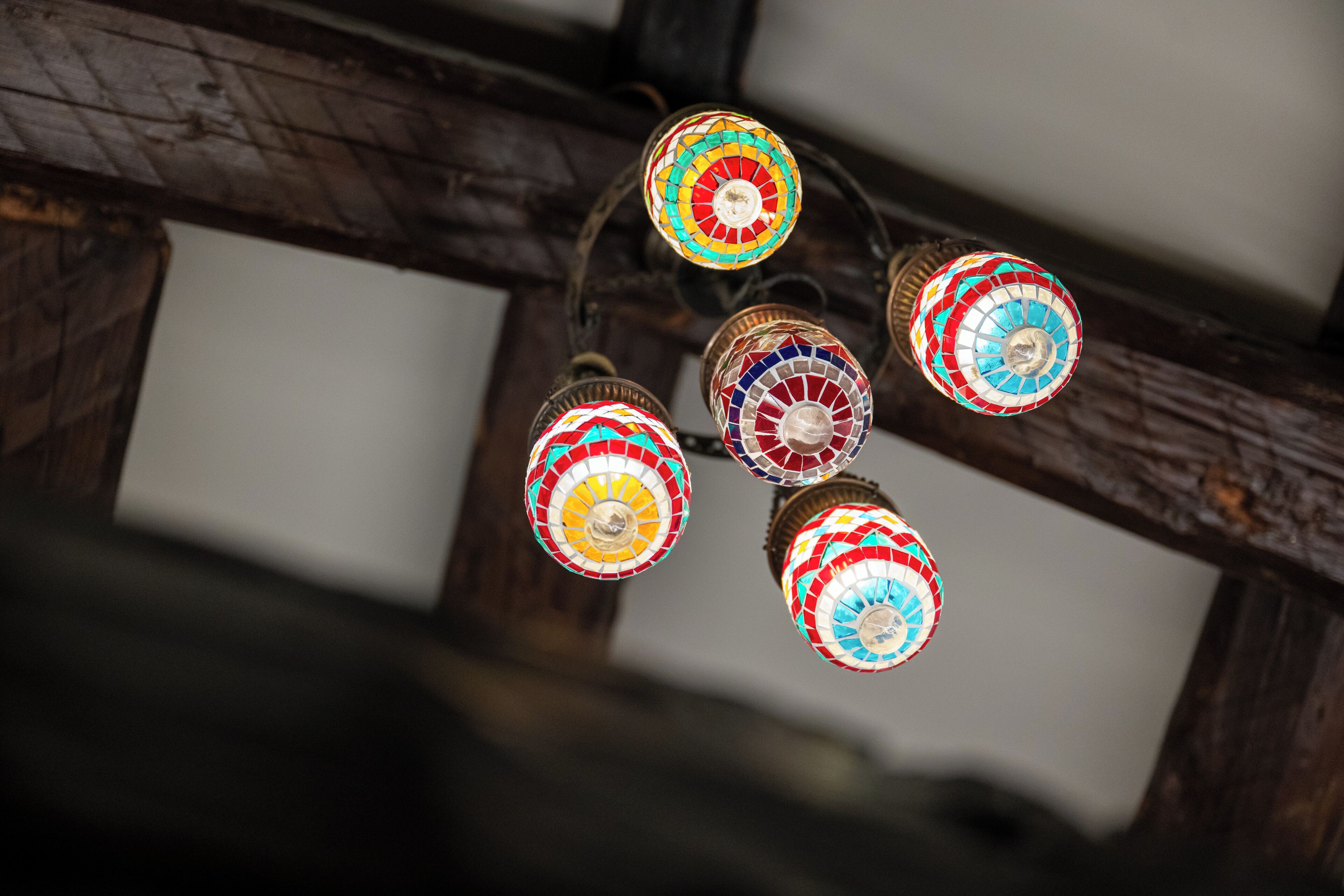 A ceiling with a wooden beam structure and colorful, mosaic-patterned lamps.
