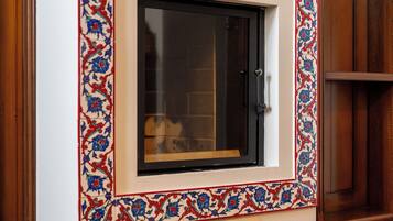 A room with a large window framed by ornate tile work, a wooden floor, and a built-in cabinet.