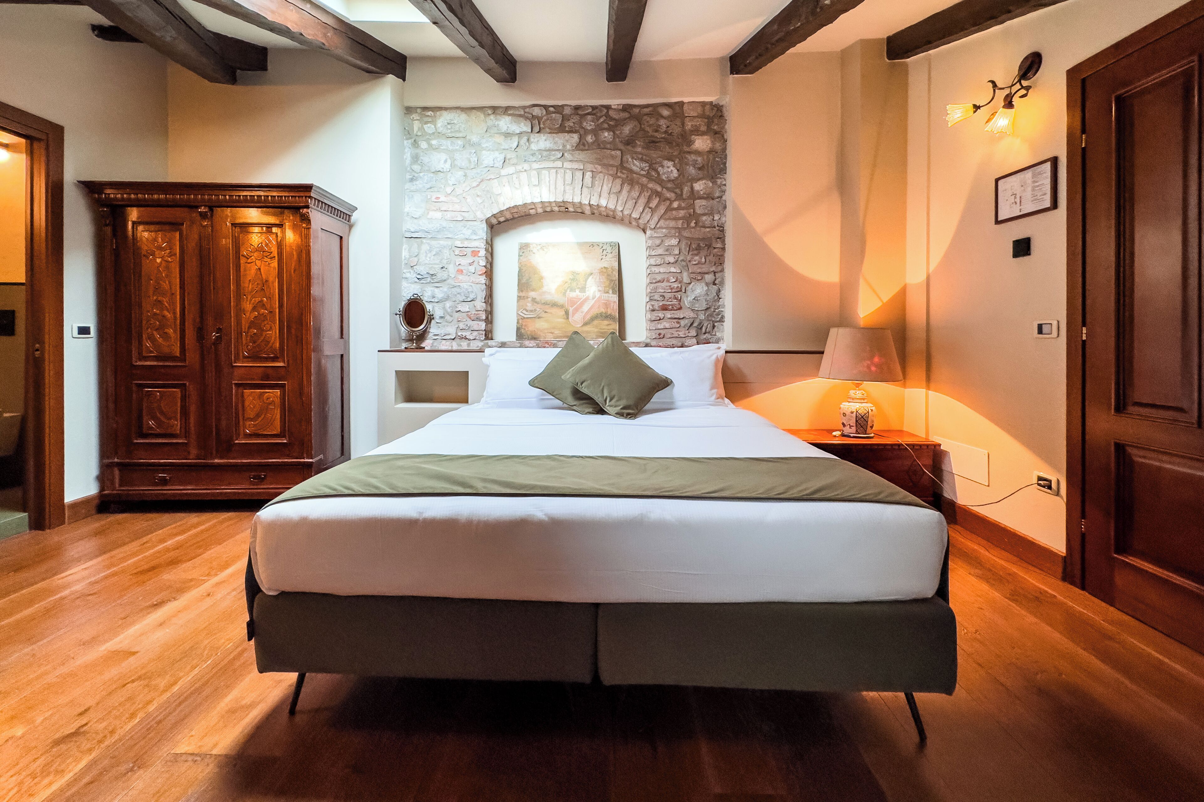 Ein Schlafzimmer mit einem großen Bett, einem Holzschrank, einer Steinwand und einem Nachttisch mit einer Lampe.