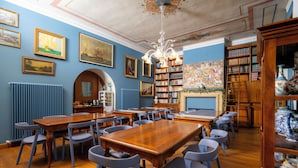 Una biblioteca con mesas y sillas de madera, estanterías llenas de libros y cuadros enmarcados en las paredes.