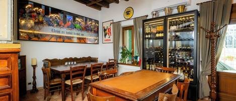 A billiards room with a pool table, wooden chairs, a bar area with wine bottles, and a large poster on the wall.