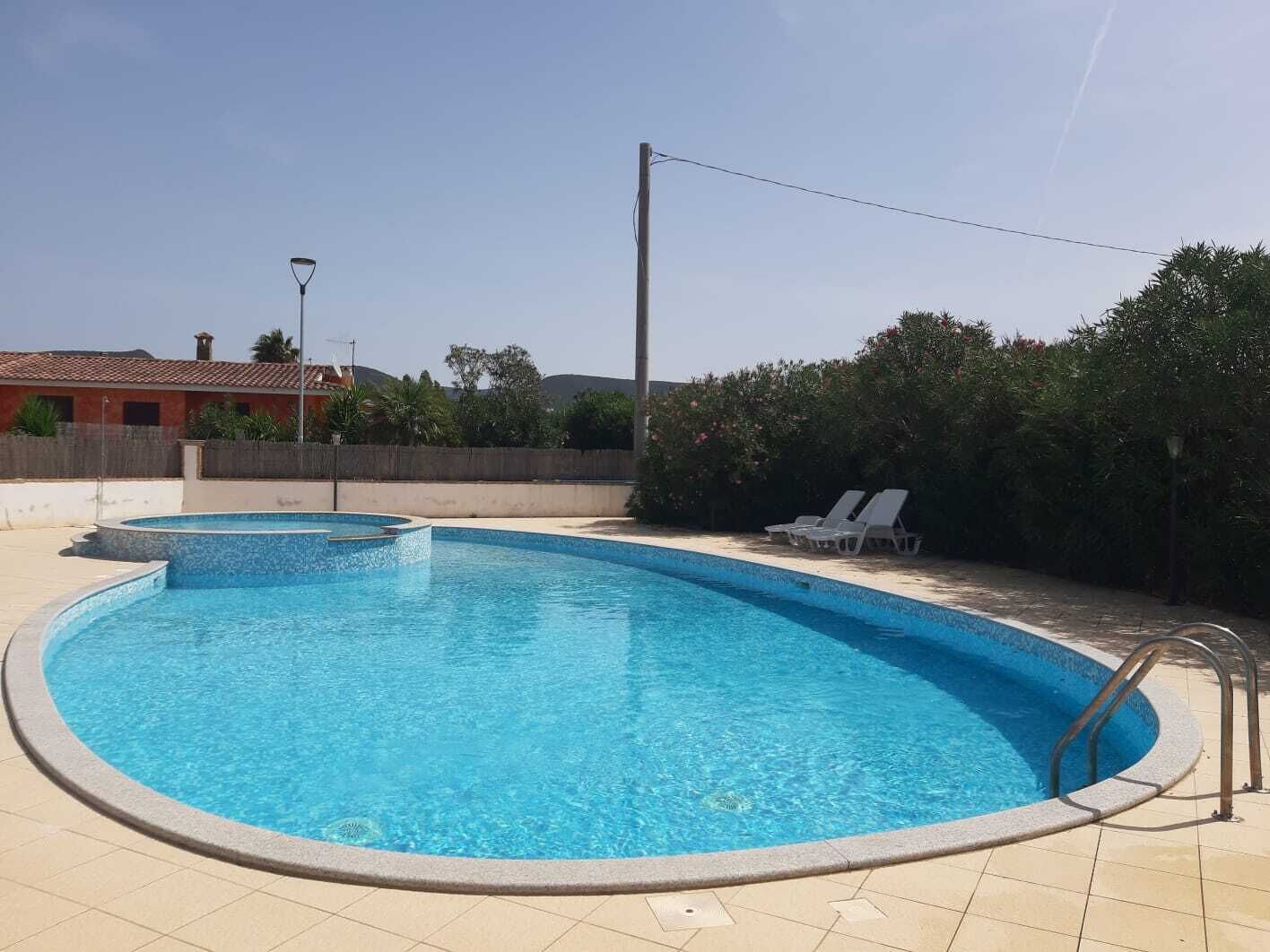 Una piscina con plataforma de azulejos, una piscina pequeña contigua y sillas de descanso.