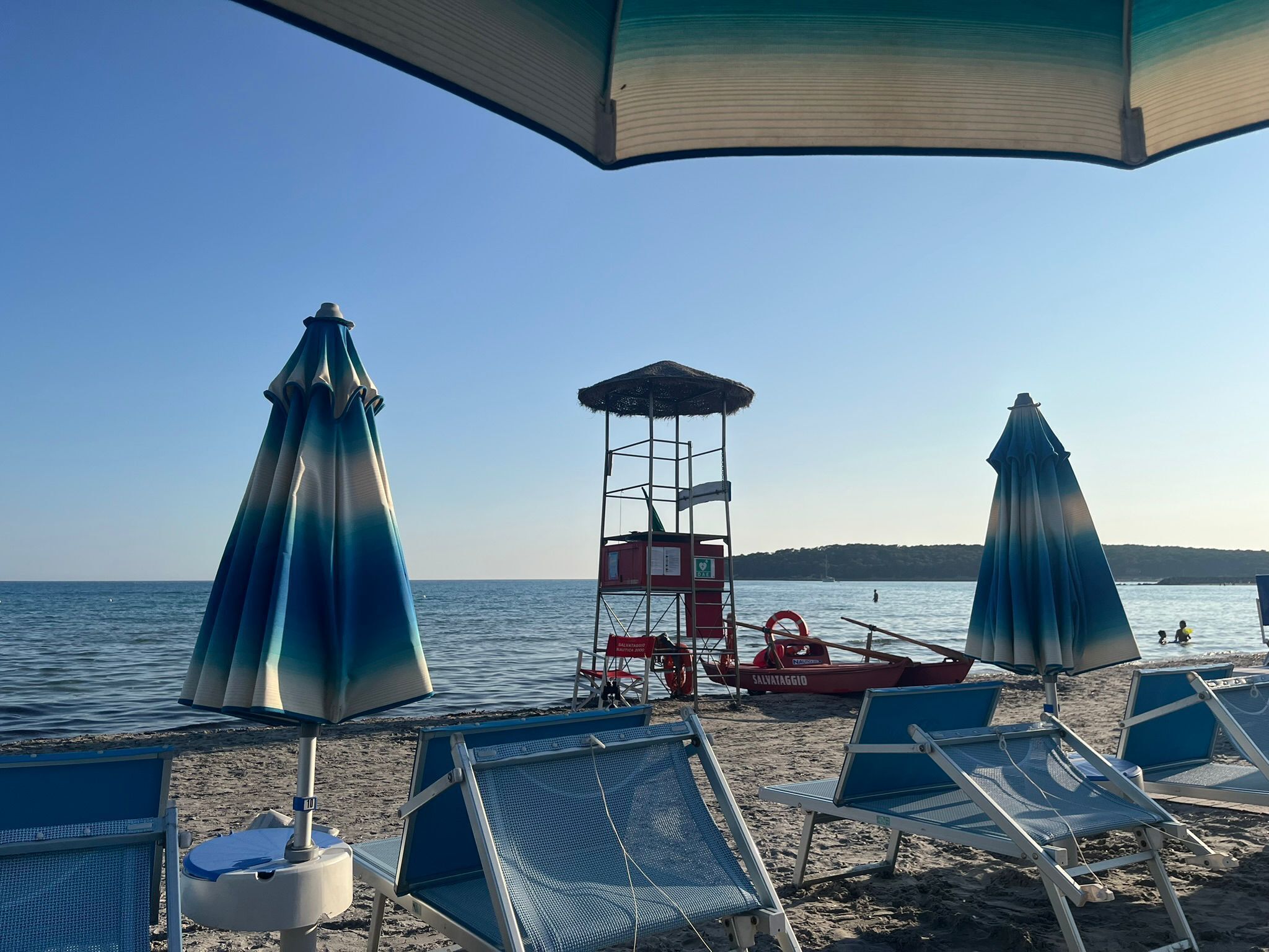 A beach with blue lounge chairs, a lifeguard tower, and a red boat.