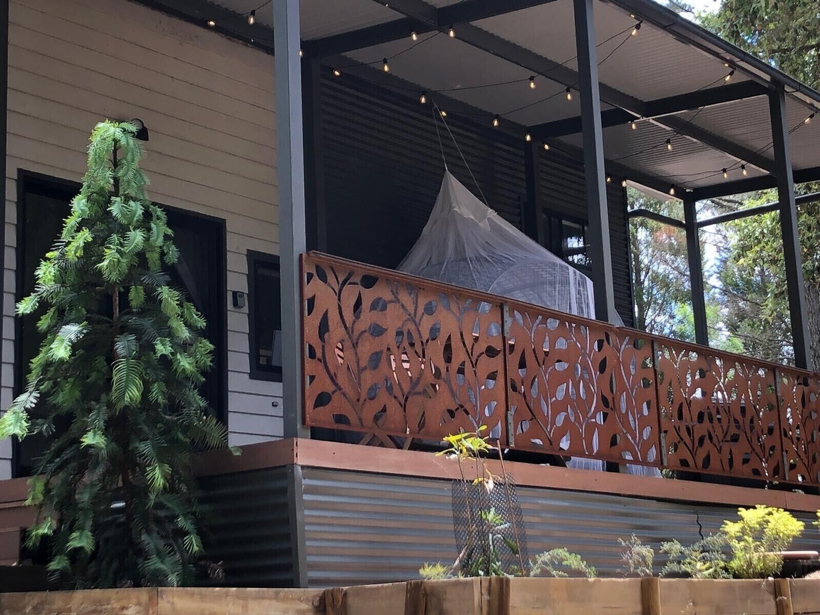 Un espacio exterior cubierto con una verja metálica decorativa, un árbol pequeño y una marquesina.