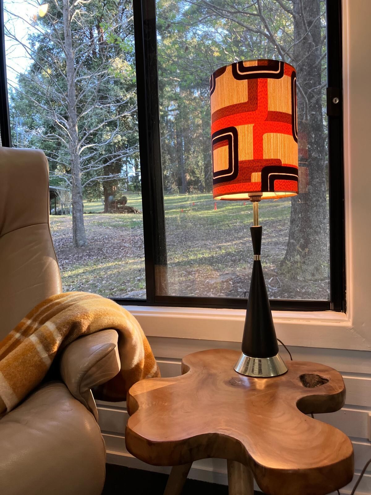 Ein Sessel mit karierter Decke, ein Holznachttisch und eine Lampe mit geometrischem Muster.
