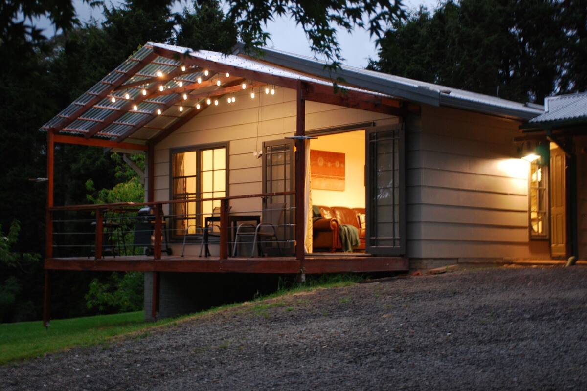 A house with a covered porch, solar panels, and a lit interior.